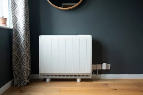 Eine Nachtspeicherheizung steht in einem modernen Wohnzimmer mit Holzfußboden und dunkelgrünen Wänden.